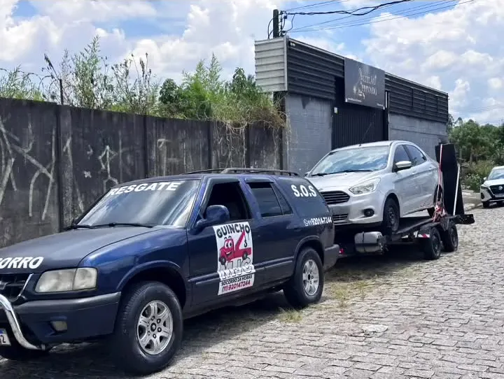 Blazer azul-escura da MJC com o adesivo Guincho MJC na porta e um hatch branco sobre a plataforma