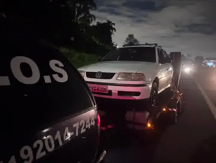 À noite, hatch branco sobre a plataforma atrás da Blazer com S.O.S e o telefone da MJC