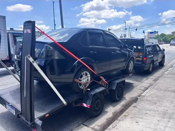 Sedã escuro sobre o reboque-plataforma, com a Blazer da MJC à frente