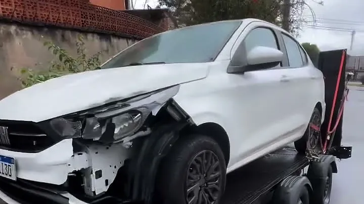 Sedã branco com a frente batida preso sobre a plataforma do guincho da MJC