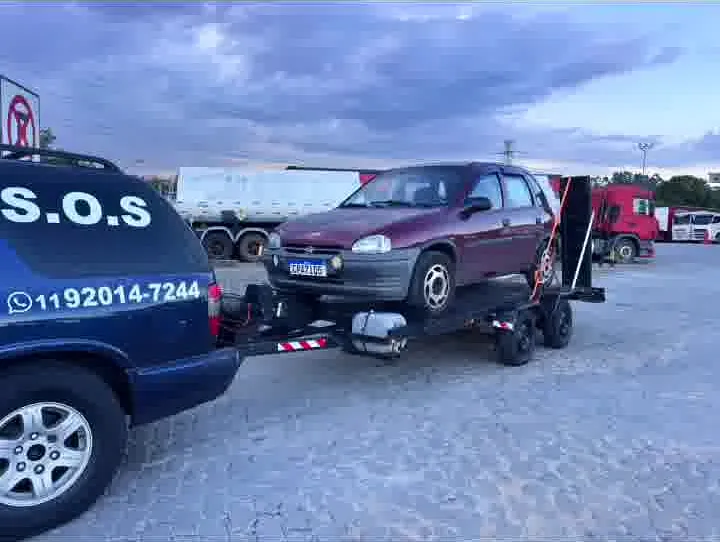 Hatch vinho sobre o reboque-plataforma, com o S.O.S e o telefone da MJC na lataria da Blazer