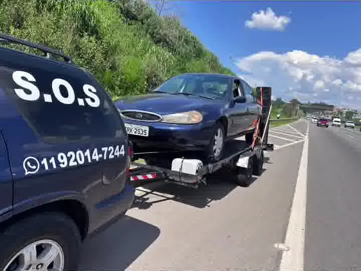 Sedã azul sobre a plataforma à beira de uma rodovia, com o telefone da MJC na lataria da Blazer
